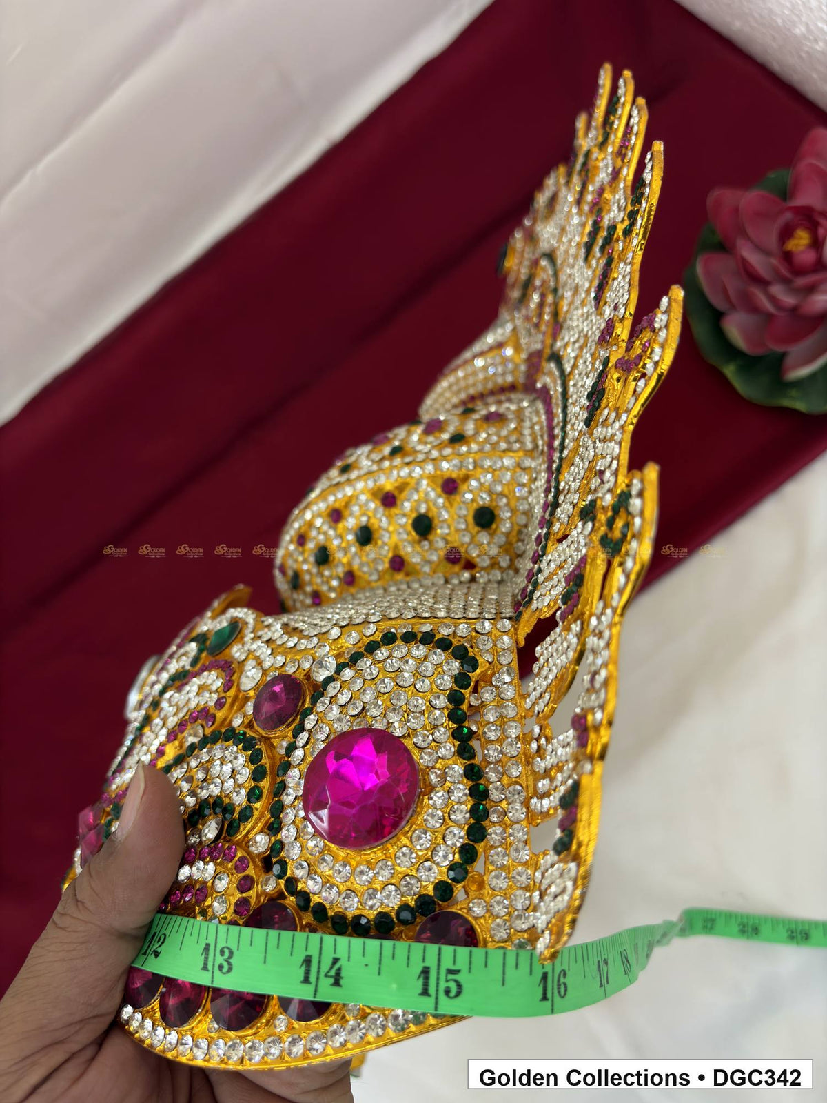 Angled side view of the deity crown showing its curved base, magenta accents and a tape wrapped around the lower band.