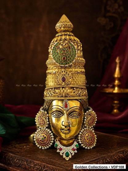 Fully Decorated Brass Varalakshmi Face with Nakshi Crown and Green Teardrop AD Necklace displayed against a burgundy devotional backdrop