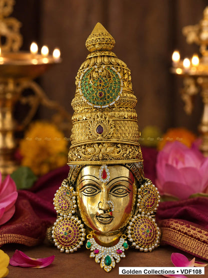 Fully Decorated Brass Varalakshmi Face with Nakshi Crown and Green Teardrop AD Necklace displayed with lotus flowers in a devotional setting