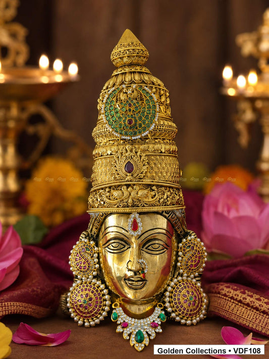 Fully Decorated Brass Varalakshmi Face with Nakshi Crown and Green Teardrop AD Necklace displayed with lotus flowers in a devotional setting