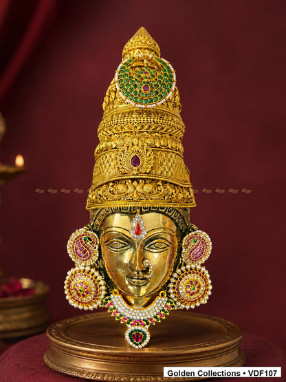Fully Decorated Brass Varalakshmi Face with Nakshi Crown and Pink Jadau Earrings displayed against a burgundy devotional backdrop