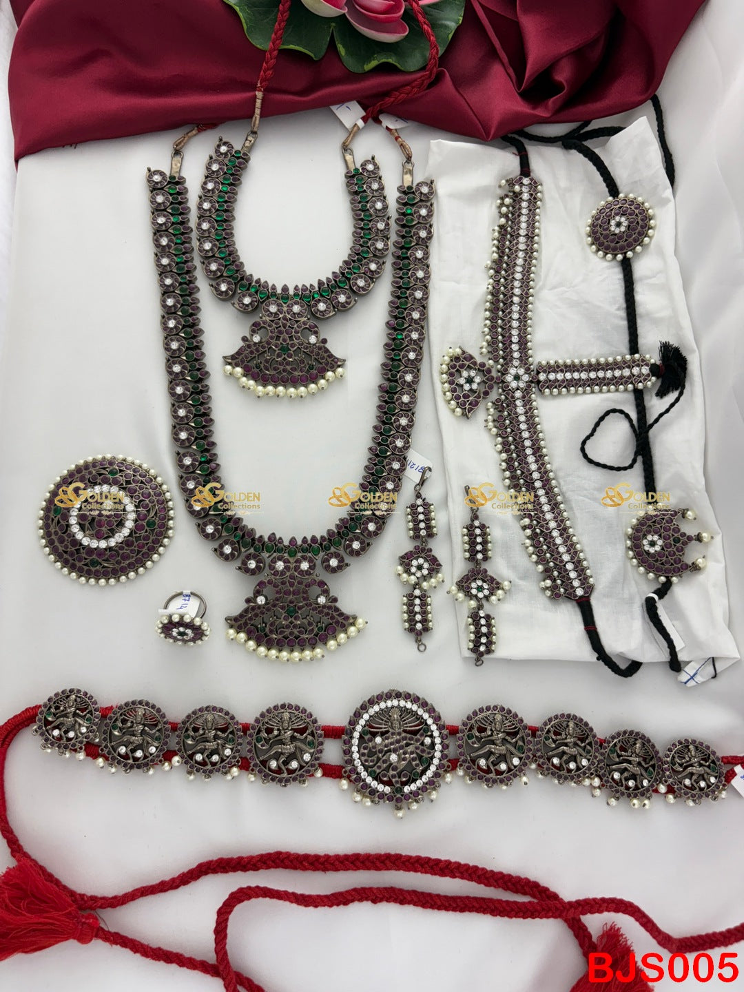 Set of traditional jewelry including necklaces, earrings, and a belt on a white fabric background.