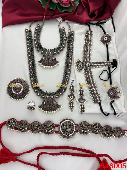 Set of traditional jewelry including necklaces, earrings, and a belt on a white fabric background.