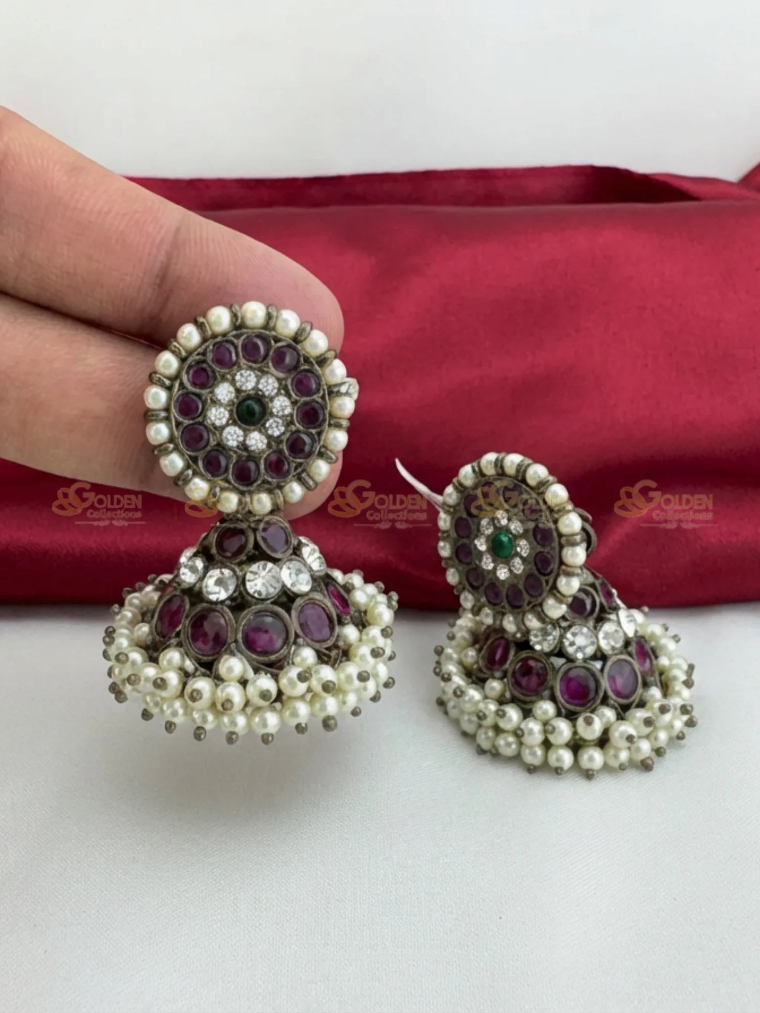 Golden Collections Kemp Black Bharatanatyam Jhumka Earrings - Pair displayed on a red silk cloth, highlighting the intricate black and ruby kemp stones and delicate pearl clusters.