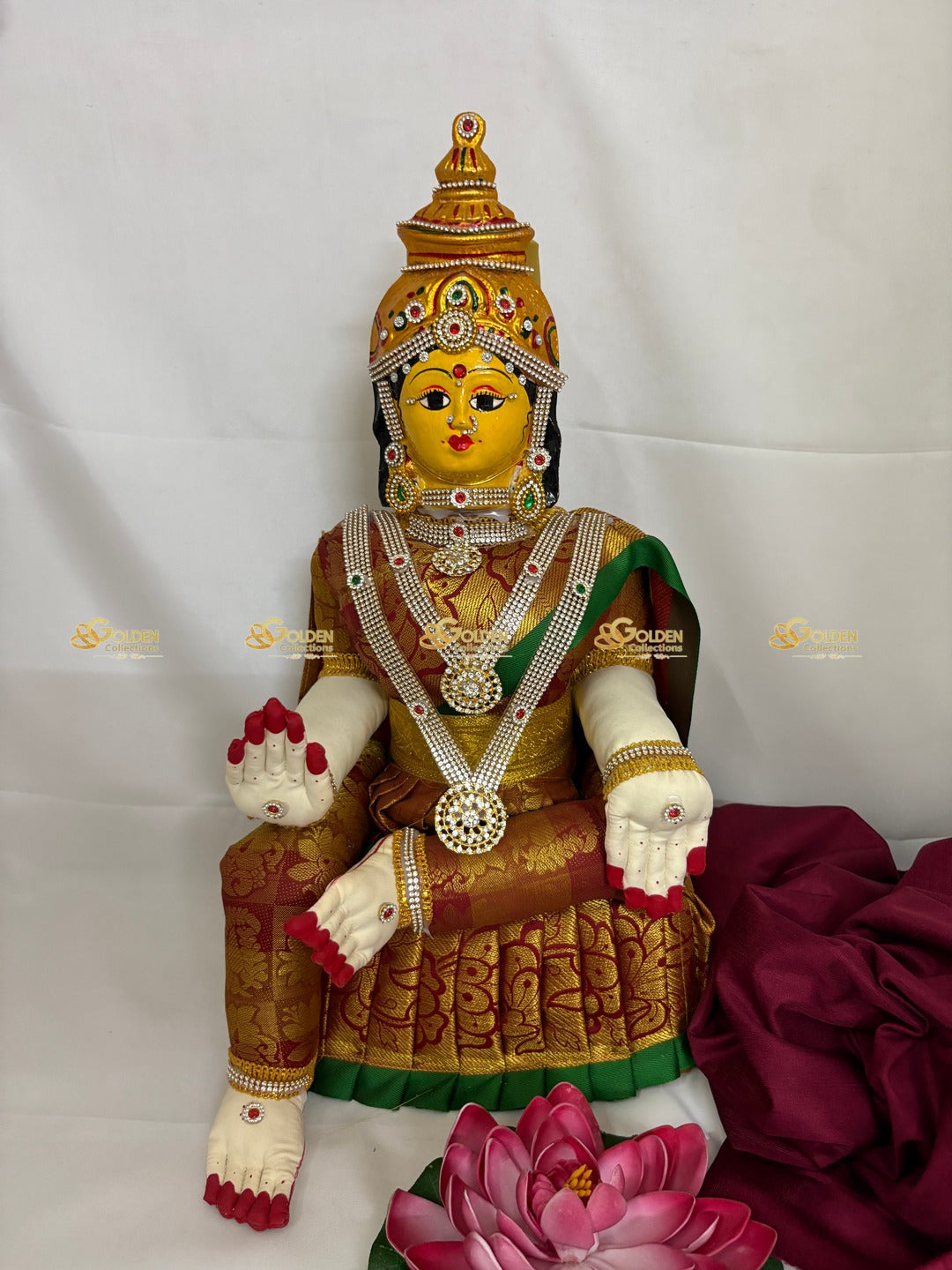 Decorative statue of a seated figure with intricate jewelry and a pink lotus on a white background
